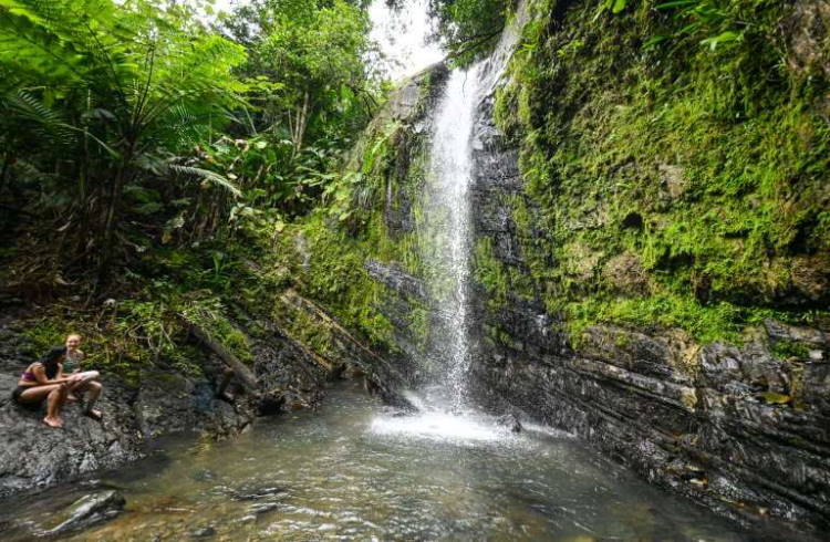 Two hikers sit beside Juan Diego Falls in Puerto Rico's El Yunque rainforest.