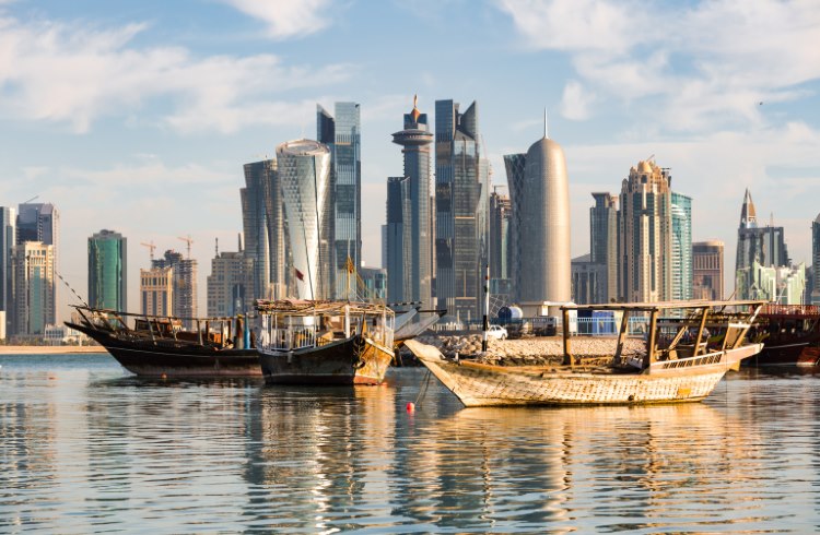 The skyscrapers of Doha's downtown waterfront, with traditional dhow boats in the foreground. 