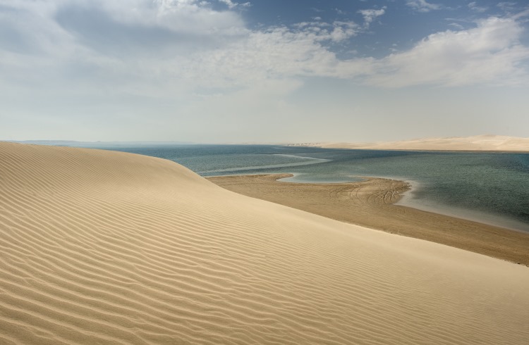 Golden dunes rise above the turquoise waters of the Inland Sea in Qatar .