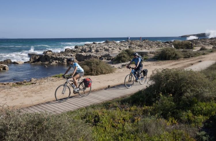 A man and woman ride bicycles beside a beach on Formentera, one of the Balearic Islands of Spain.