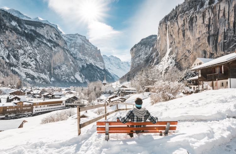 A man sits gazing at the Swiss village of Lauterbrunnen, set in a scenic valley.