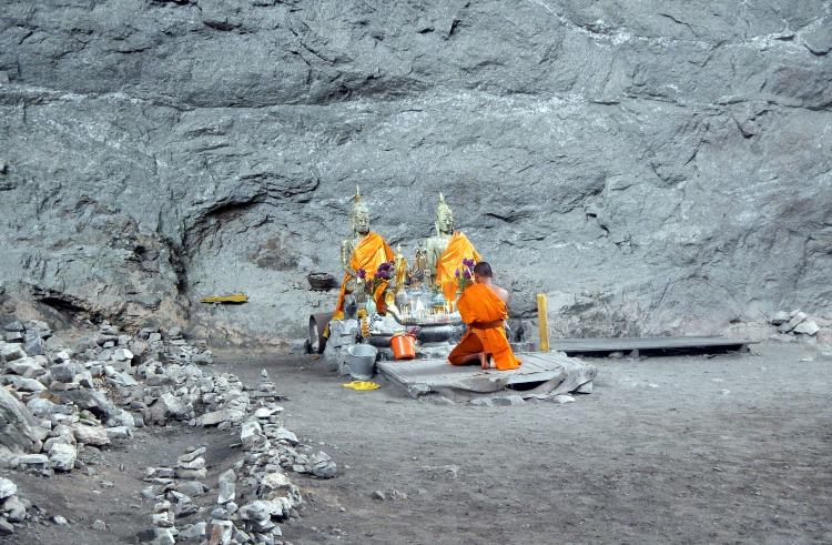 A buddhist monk kneels before a small altar in Tarn Lod Yai cave, Thailand.