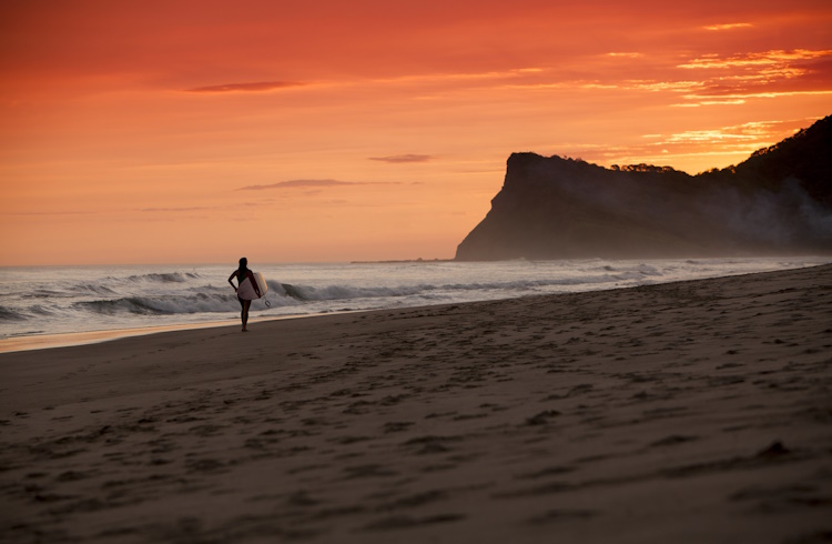 A surfer carries a surfboard along a secluded beach in Nicaragua.