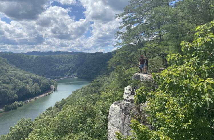 Hikers stand on a tall cliff overlooking New River Gorge in West Virginia, USA.