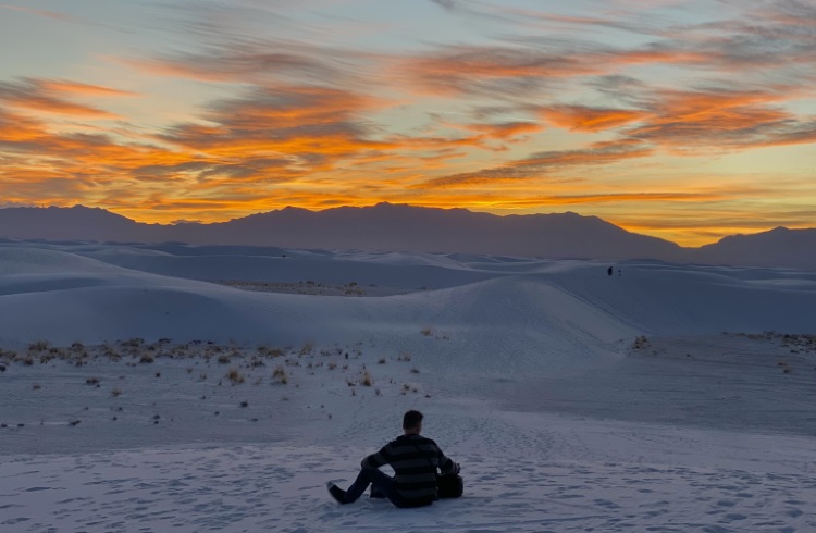 A man sits watching the sunset over the dunes at White Sands National Park, New Mexico.