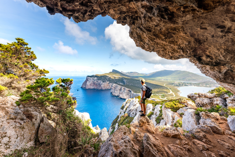 A man standing at the mouth of a cave looking over a bay
