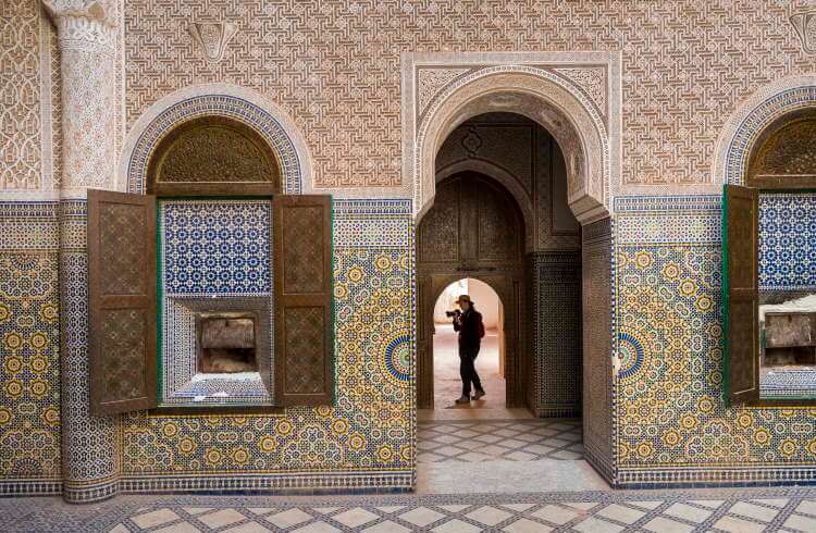 A photographer walks through an ornately tiled building in Morocco.
