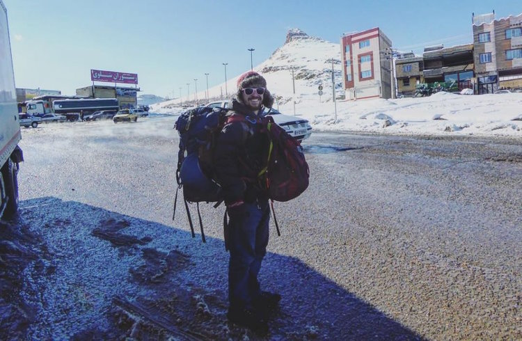 A backpacker in a snowly landscape smiles at the camera.