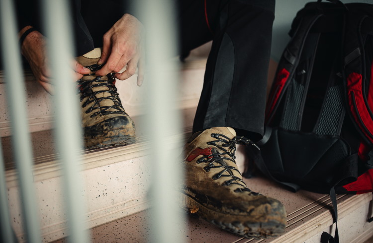 A man ties his hiking boots while sitting on a flight of stairs.