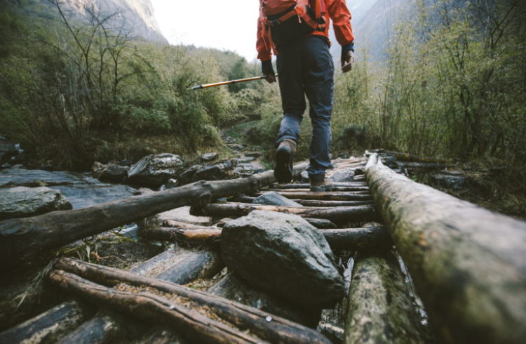 A male hiker crosses a log bridge over a stream.