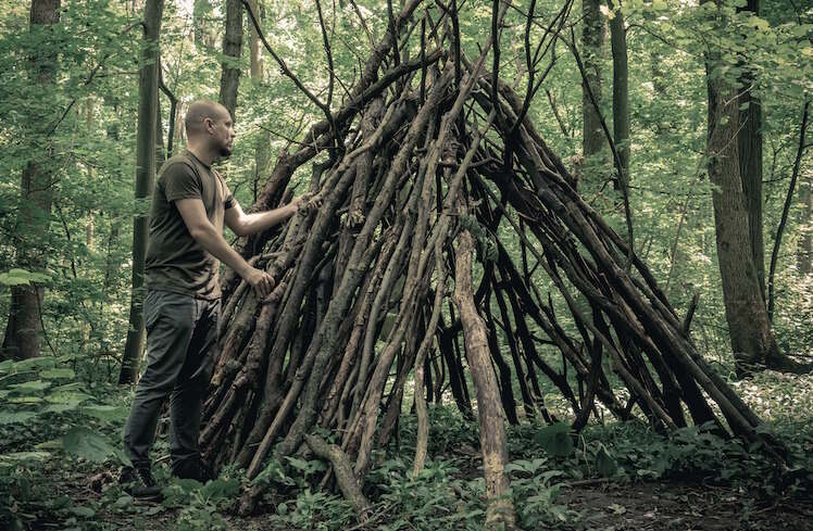 A man builds a makeshift shelter out of large sticks.