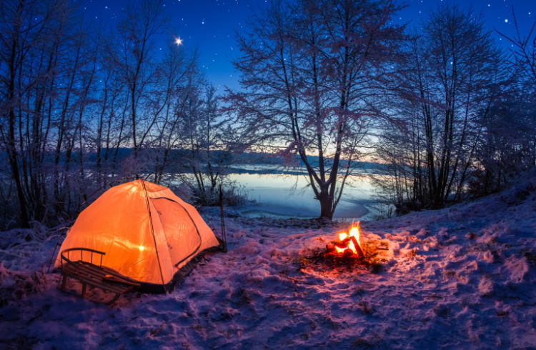 A snowy campsite with a campfire at dusk.