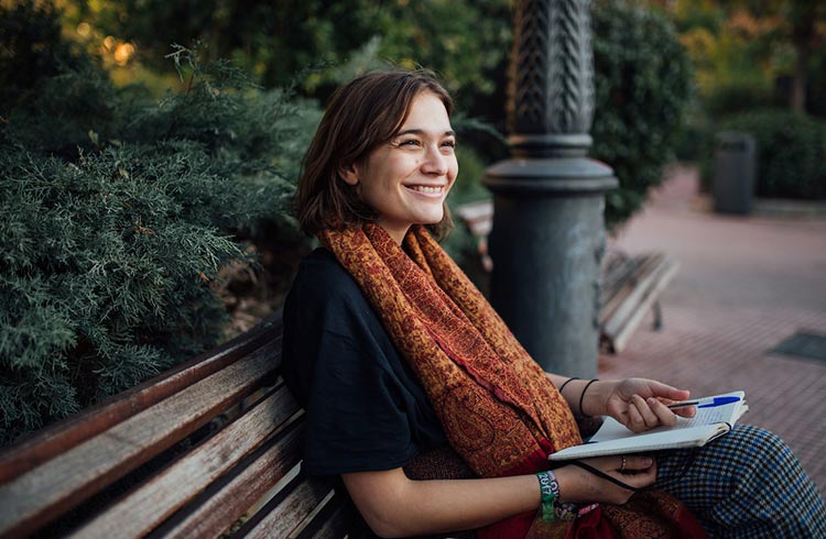 A young woman writes in her journal on a park bench in Madrid, Spain