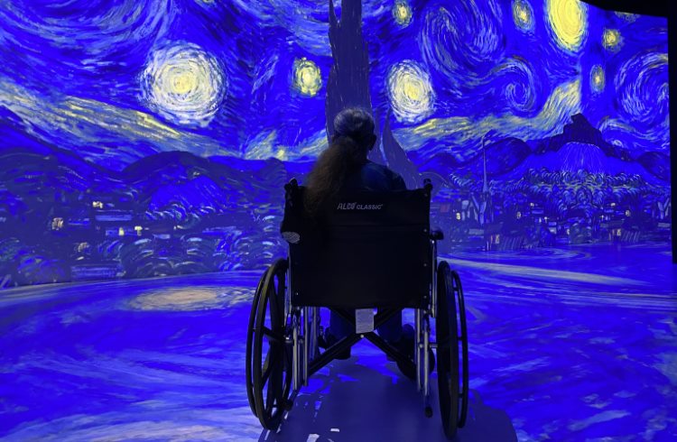 A woman in a wheelchair enjoys an immersive Van Gogh exhibit at a museum.