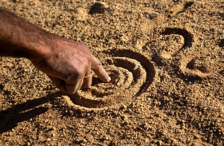 A close up of an Aboriginal man's hand drawing the dreamtime stories in the dirt