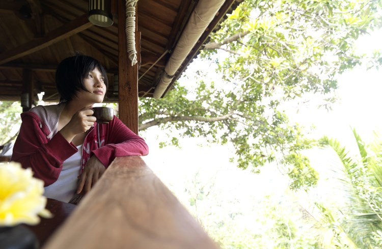 A woman sips coffee on the deck of a jungle lodge in Bali.