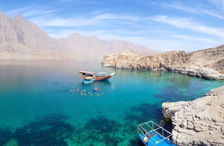 A group of swimmers swim alongside a traditional boat in the Oman fjords.