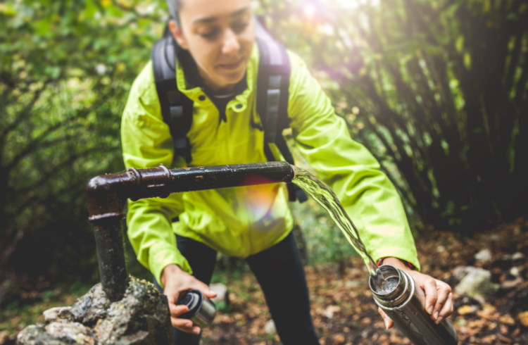 A hiker refills a reusable metal water bottle.