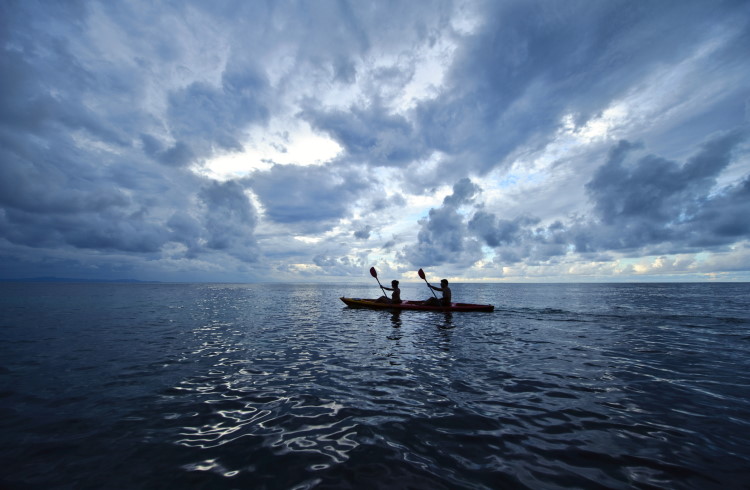 A couple kayaks across a calm ocean in Fiji.