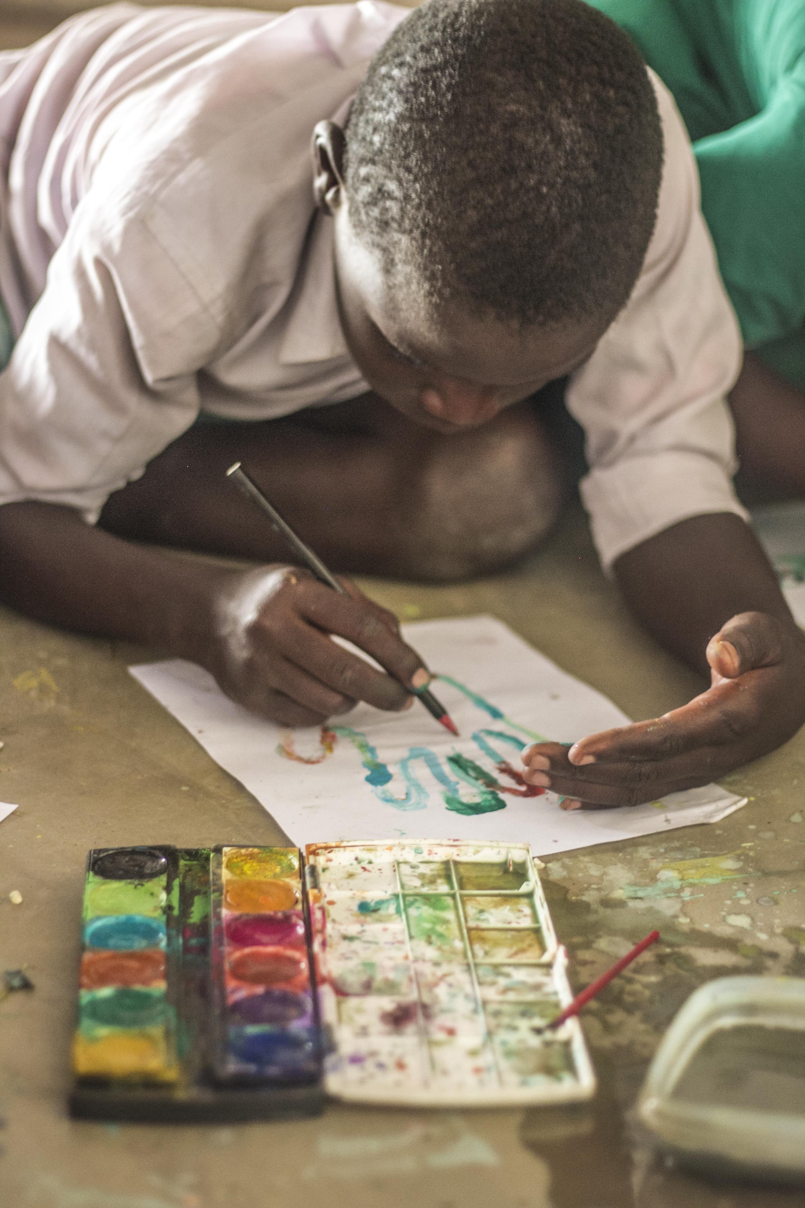 Ernest, age 10, is a Standard Three learner and is using paints for the first time.   Volunteers often bring donations to Mlambe school from abroad and hold extra-curricular activities, ranging from painting and drawing to physical activities.  