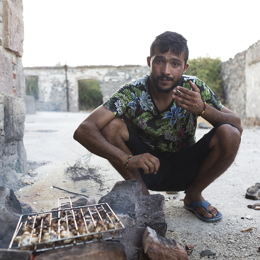 Haji making a barbecue for other refugees from the Squat in Lesvos while smoking. 