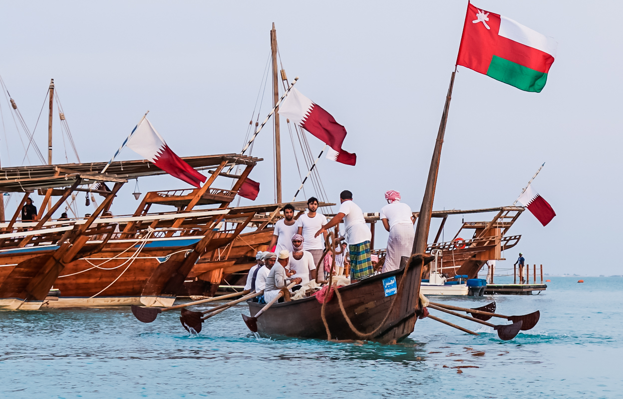 Qatari and Omani flags are proudly displayed together on this traditional dhow boat as the men unite and deploy their fishing nets into the Persian Gulf.