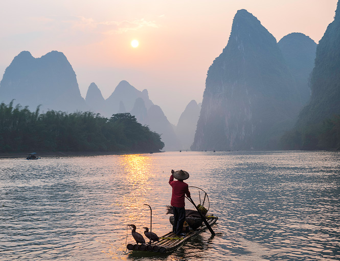 A Chinese fisherman with his Cormorant birds paddle off on the Li River in Xingping, China.