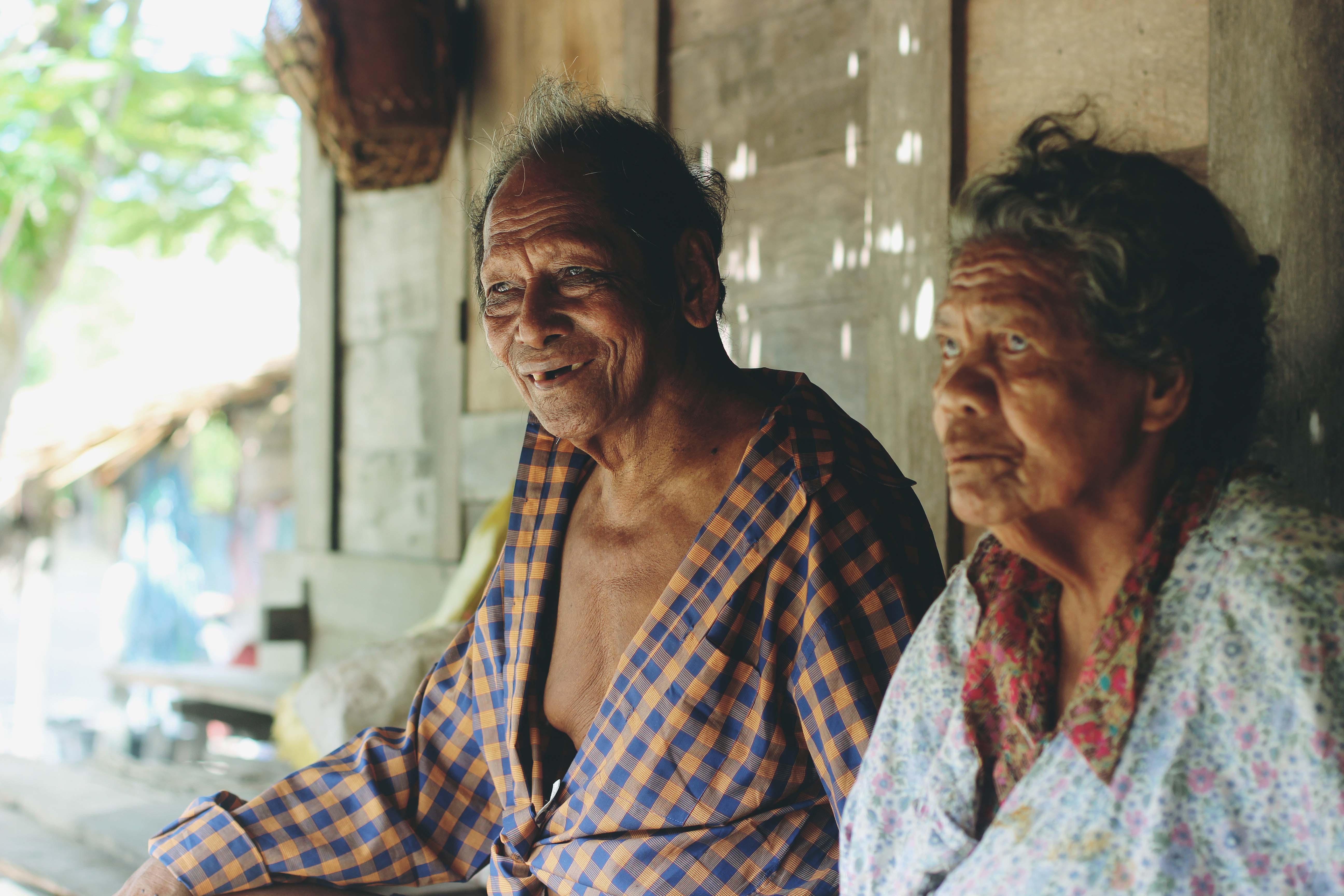 Grandfather and grandmother, two elders of the upper village, sit on the front porch of the house they were born in. The upper village is built on a hill that was traditionally only accessible by wooder ladders. Only a few traditional houses, made of wood and palm tree leaves, remain. Beliefs are deeply rooted within the spatial organisation of the village itself, with spaces devoted to the spirit world, often at the back of the house, where speech and other worldly activities become taboo.