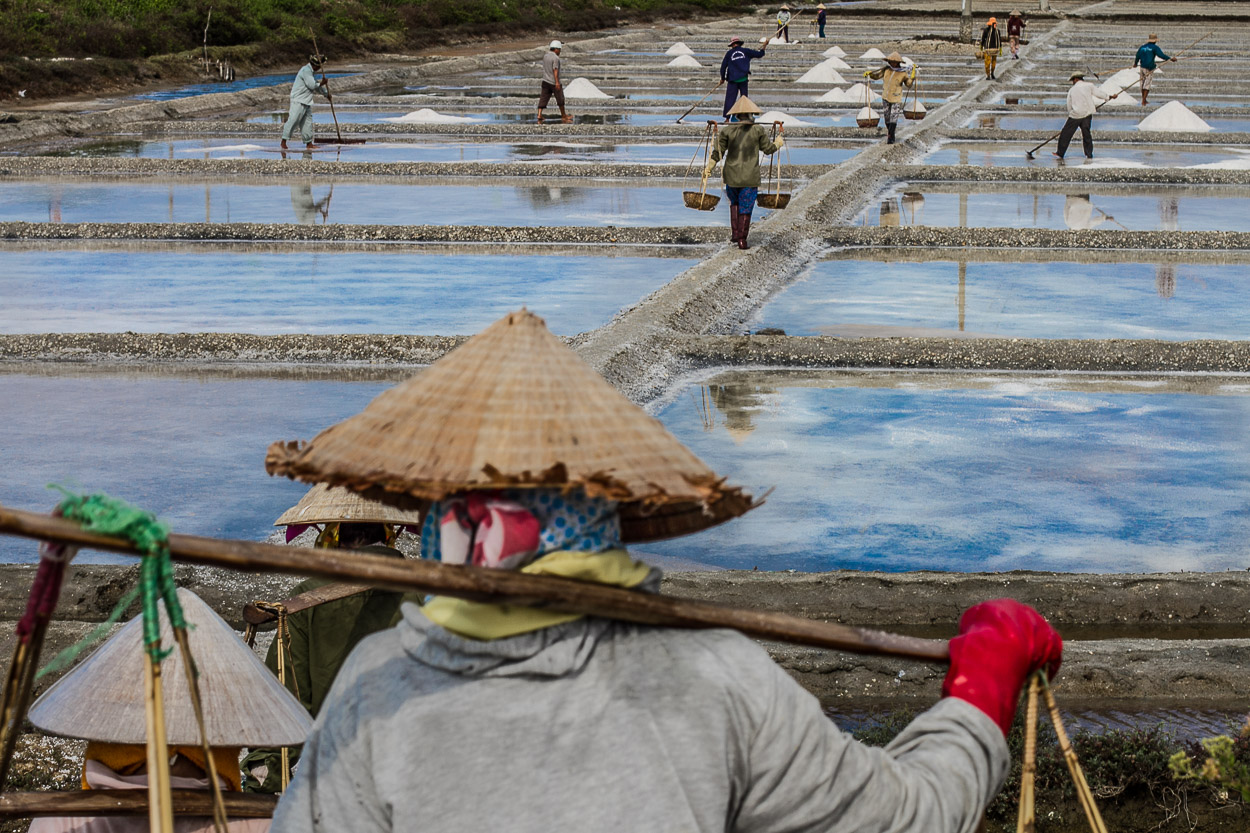 Vietnamese working in salt works, producing salt through from the evaporation of seawater process. Somewhere near Hoi an city, Vietnam.