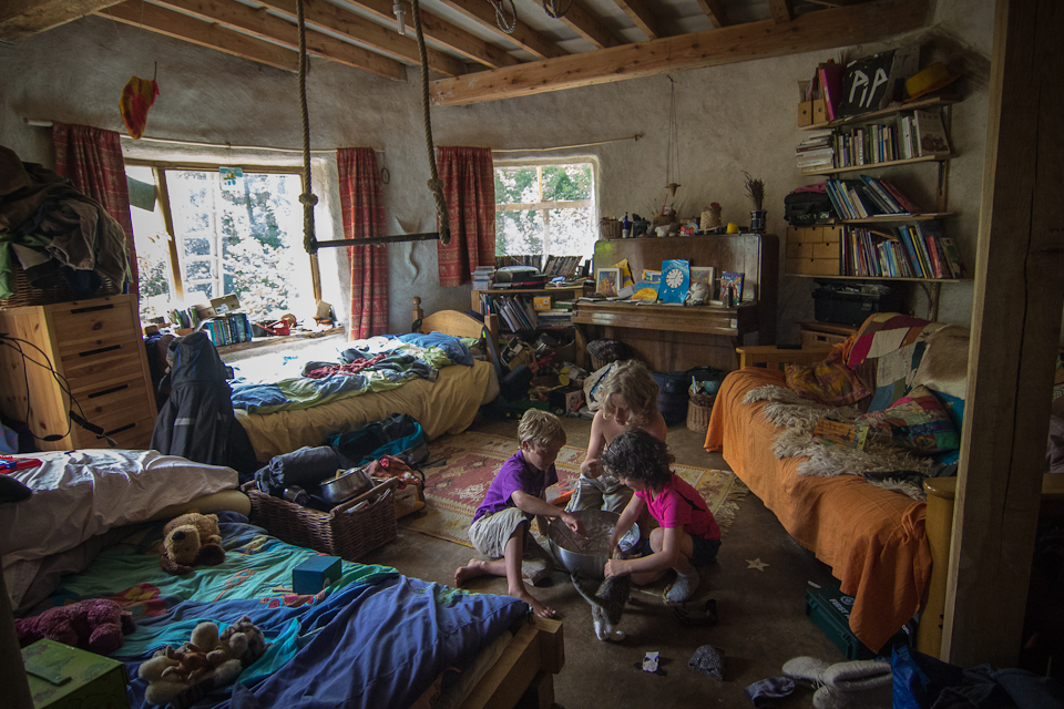 Inside one of the houses, Alice Mattioli, Pip and Louie Whittaker clean out a cake bowl, assisted by Pirate, the cat, July 2013. The house has no dividing walls so the entire family uses this one big room as bedroom, living area and playroom. A trapeze hangs from the ceiling.