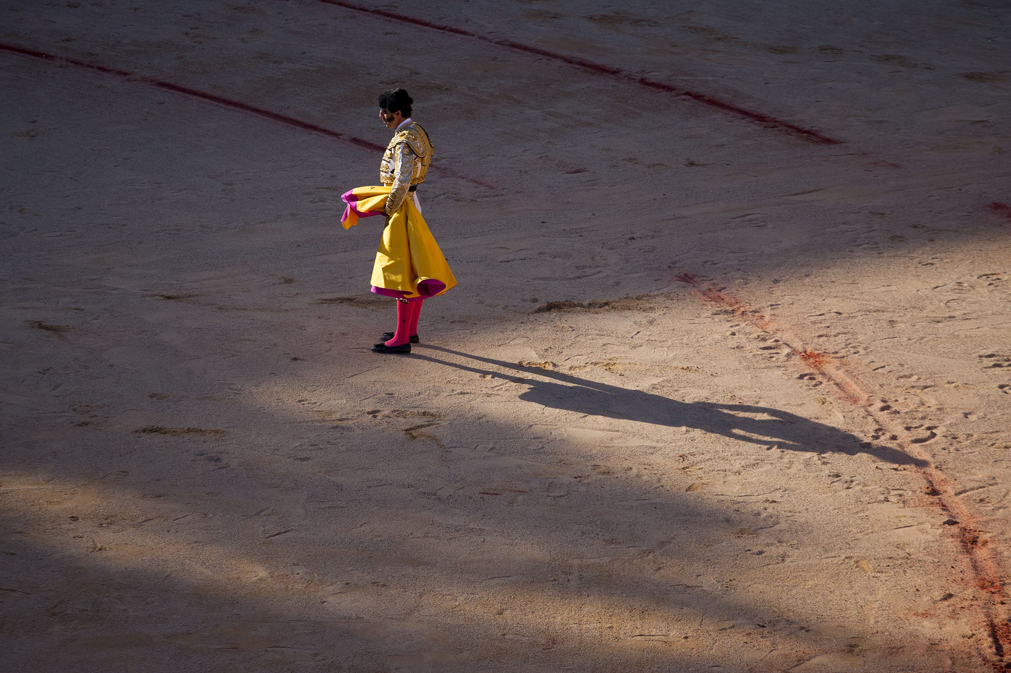 Padilla, a famed bullfighter who once lost an eye to a horn, stands alone as the sombra section of the bullring grows. He sports the suit of lights but also the cape used by the aides-he's performing the entire bullfight on his own.