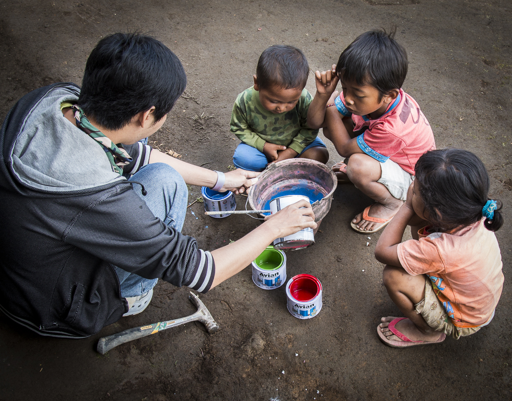 A member of the Habitat Indonesia team is assisted by the children.  Paint is mixed with cement water to be used on the lower third of the walls of the houses.  This provides a water proofing layer around the base of the house and provides some decoration to the concrete block construction.