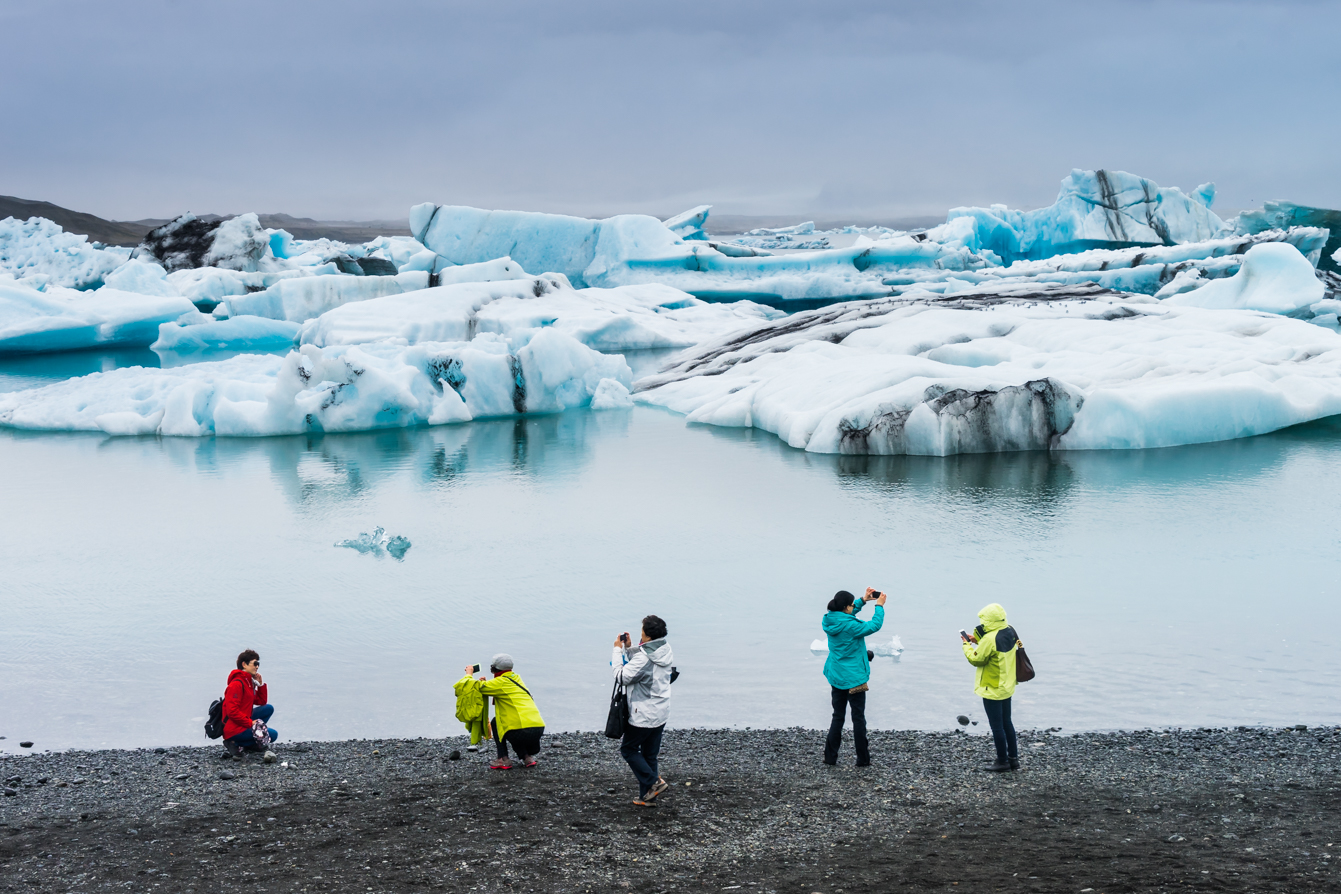 Tourists taking photos in front of the glacier lagoon lake. A fantastic world for them, completely different from what they are used to.