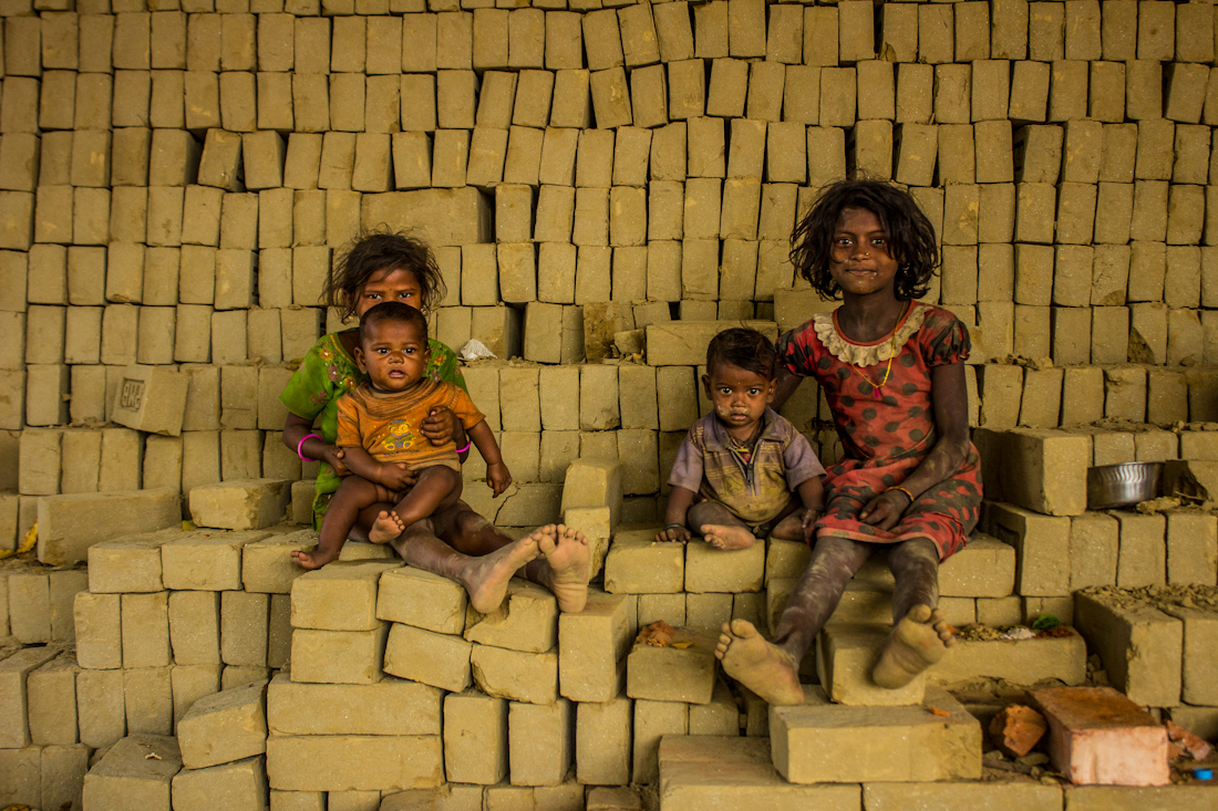 Every day of the year excepting the rainy season in remote villages all over India, groups of families gather in communities to make bricks at large factories. Complete generations together take charge of the whole factory production making this work their lifes. This is a view of just one of these factories and its people.  (In this image: kids resting over bricks after breakfast).
