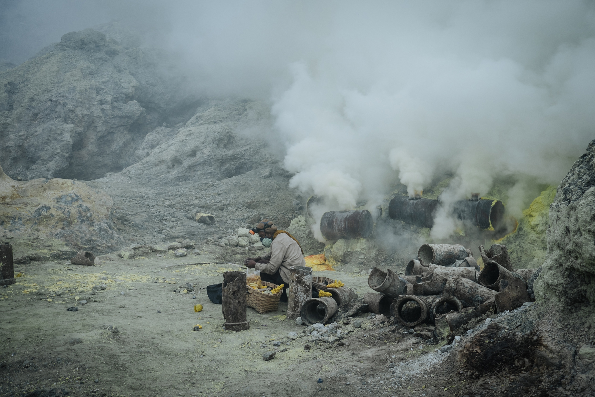 A miner works to break up the bright yellow rocks of Sulphur after it spills out of ceramic pipes. These pipes channel the volcanic gases, condensing them to form solid sulphur.
