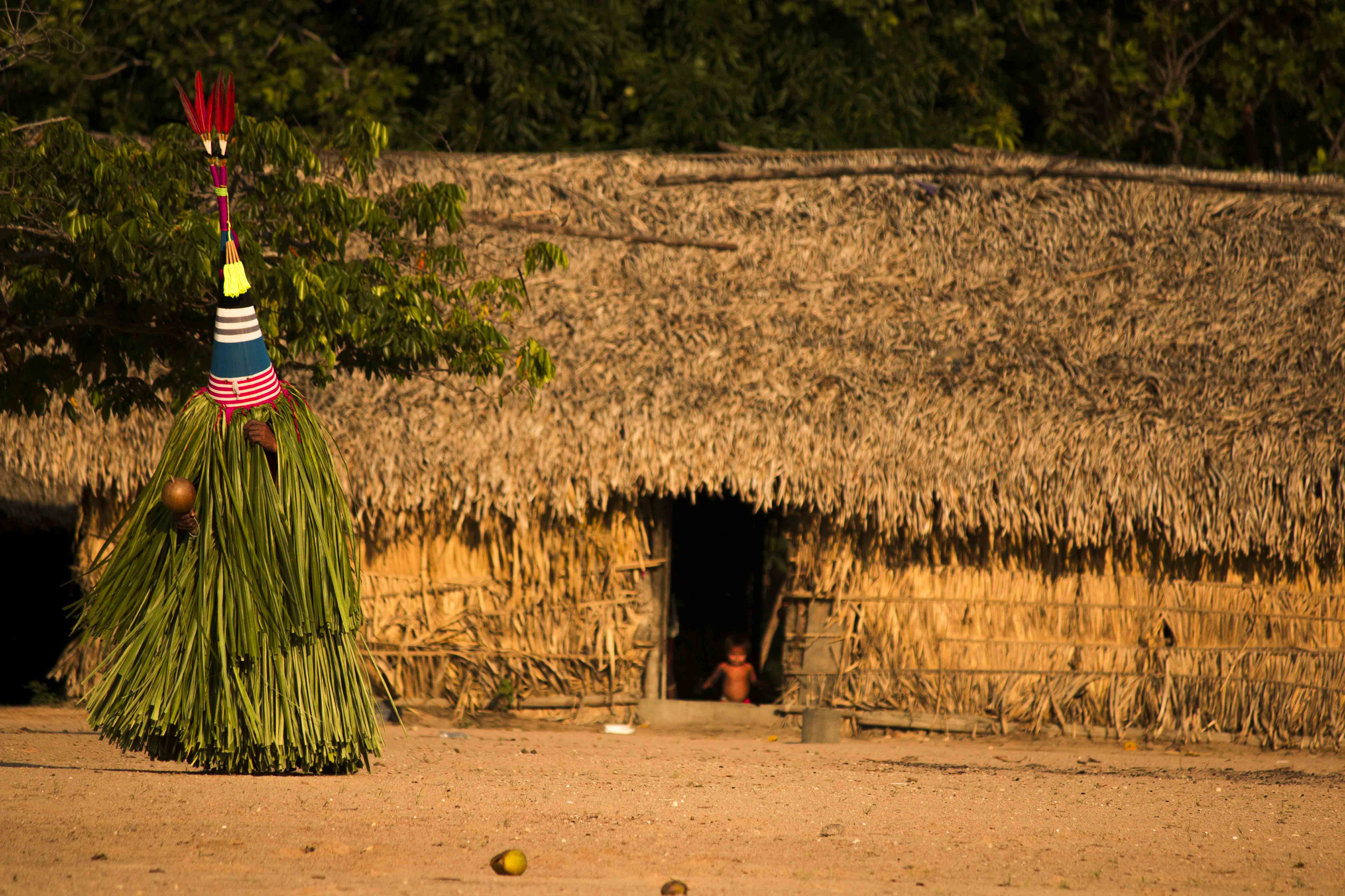 A man performs a traditional dance, while a young child stands at the doorstep, unaware of what is happening.