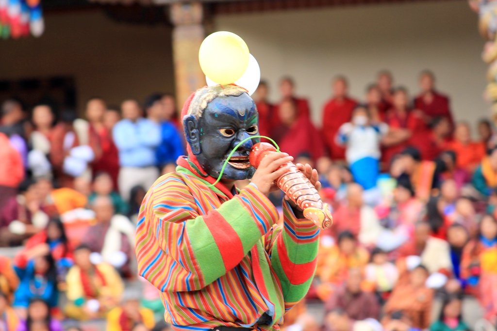 'Atsara', the humorous masked man, entertaining the audience with a "Phallus" (Wooden Penis). He's trying to represent his toy as a flute, in order to make people laugh.