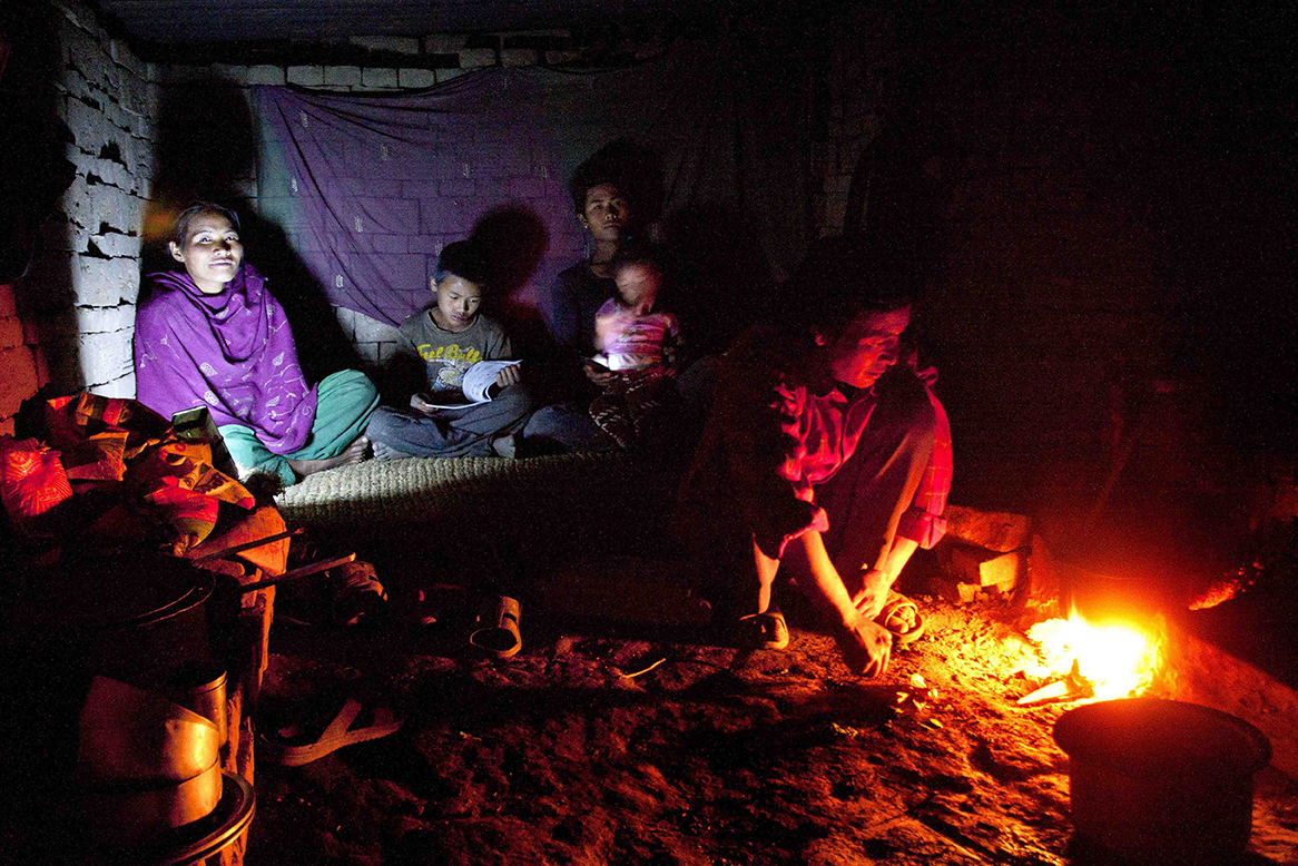 Padam Bahadur Tamang prepares dinner for the family inside a temporary hut in brick making fields in Nalinchowk, Bhaktapur. Padam's son, Dawa, 11, reads other members of the family take rest. During winter Dawa accompanies his parents to the field while during summer he goes to school back in the village.