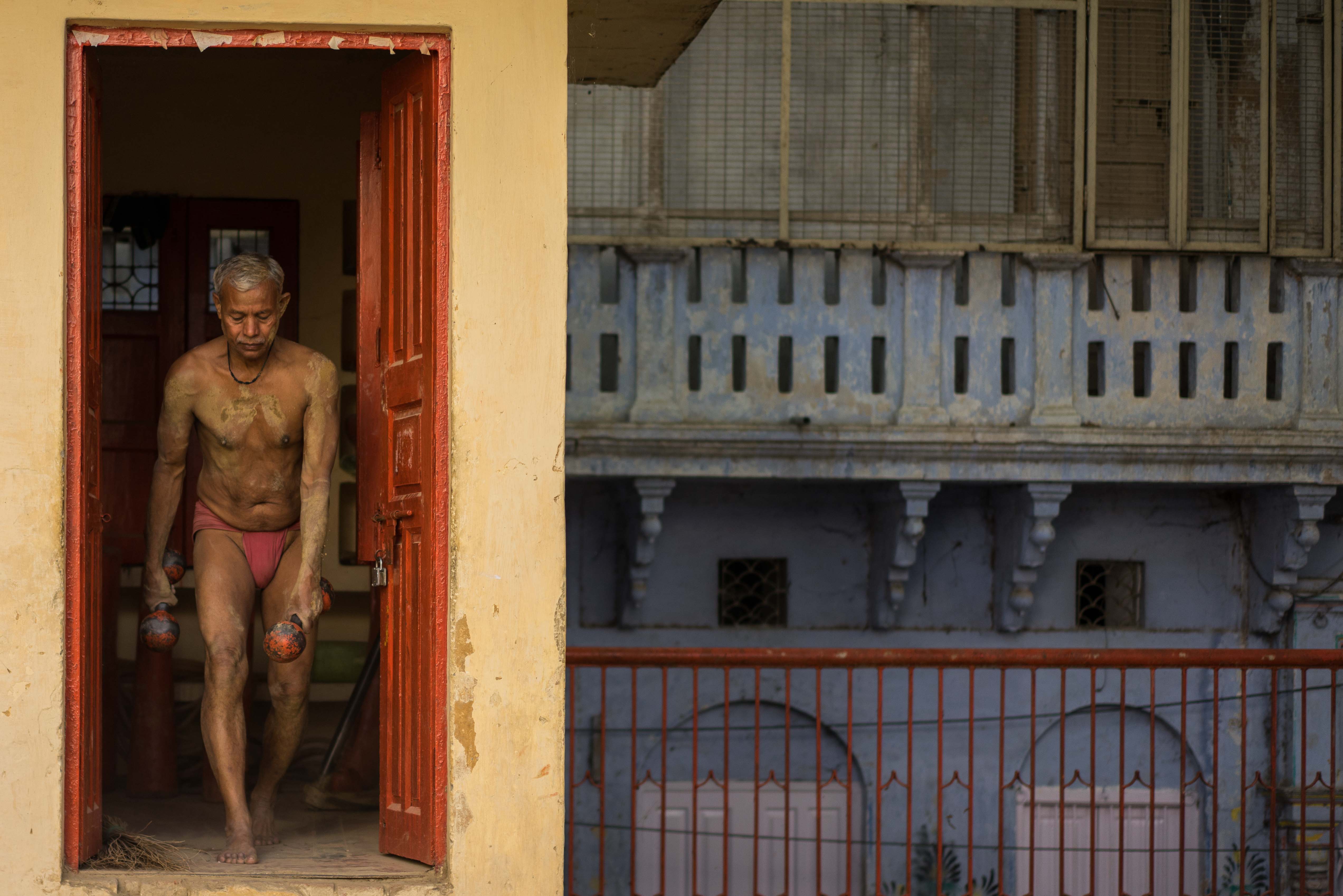 An elderly Kushti wrestler walks out with some weights in preparation for an early morning training session.