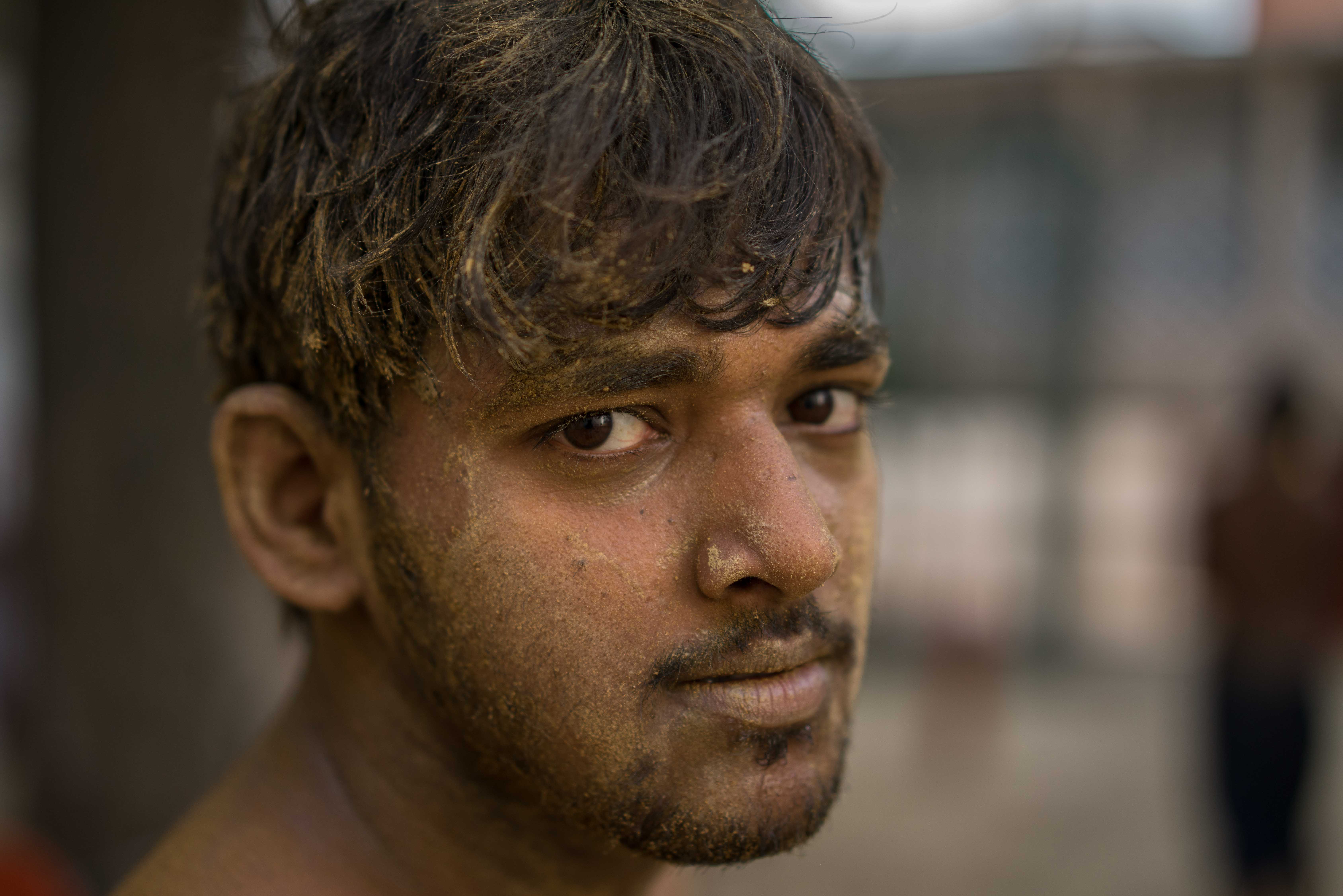 A young Kushti wrestler covered in dirt reflects on a tough training session.