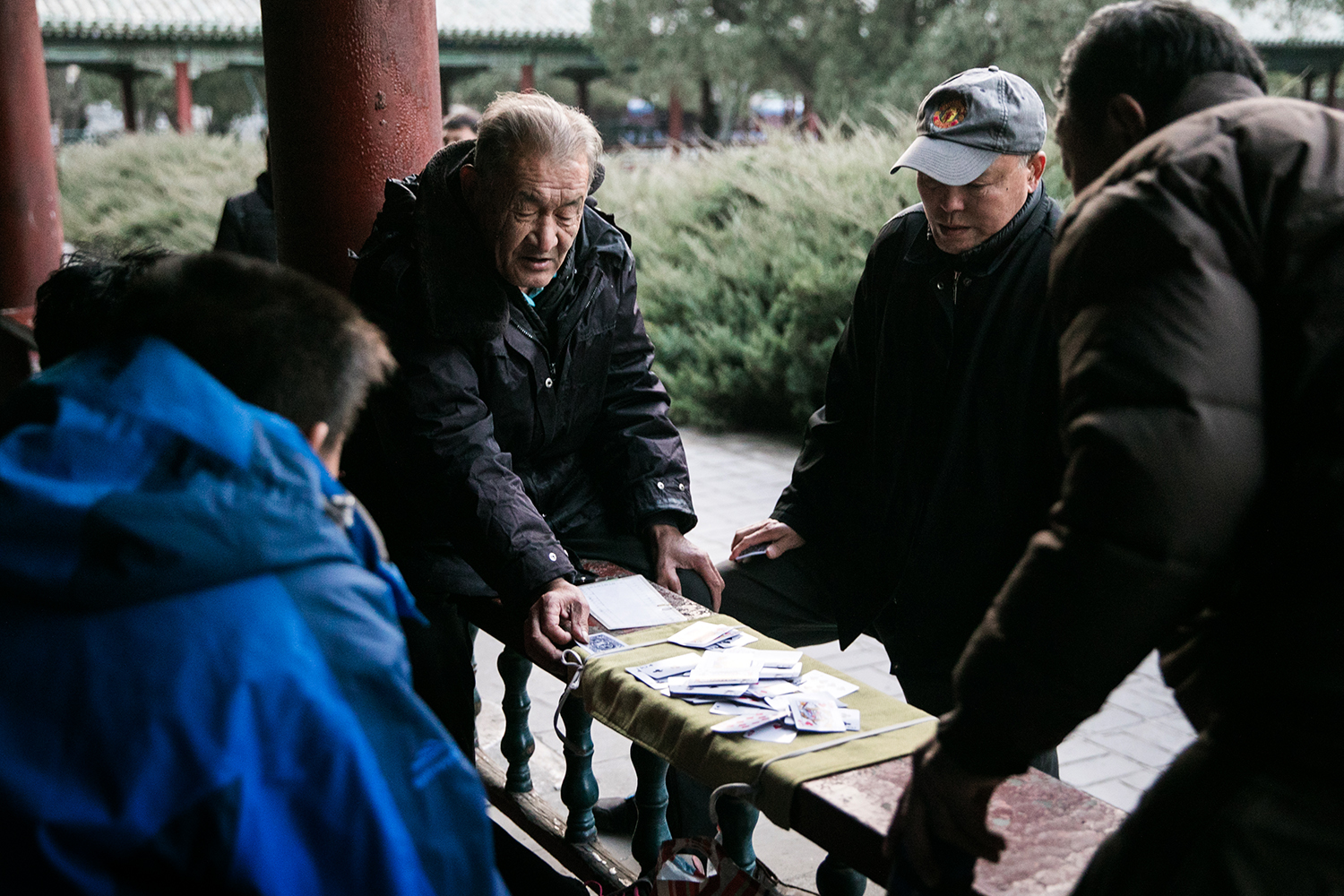 An elderly man lays down his cards to play as two young boys watch intently. Even with new technology, there is a sense of value in a more simplistic way of leisure time, and it goes beyond generations.