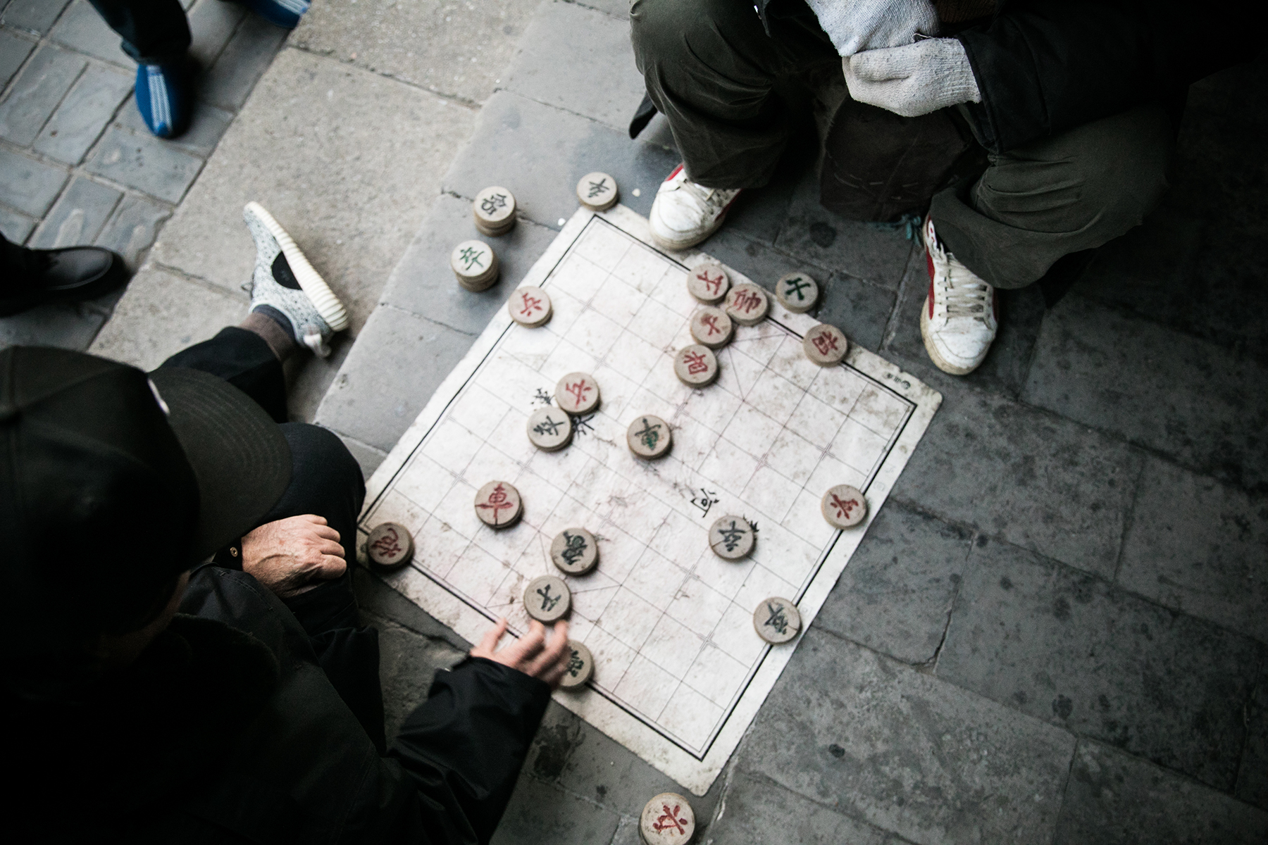 Two men play a game of "Xiangqi" on the Temple grounds - quite literally placing their playing mat on the concrete. Spectators watch eagerly over their game play, with the low angle of the board giving them the best view.