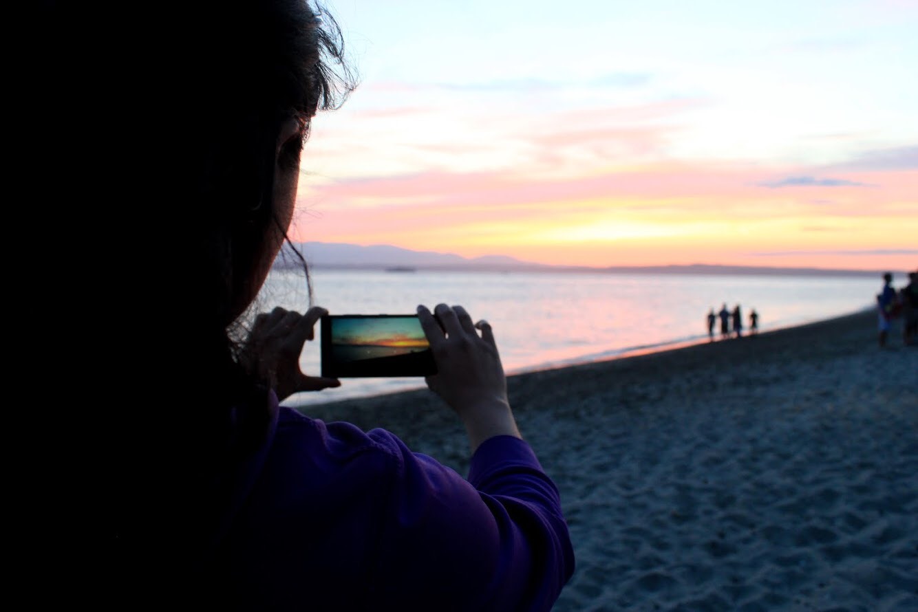 A member of Unidas Seremos captures a picture of the sunset at Golden Gardens Beach on her phone.