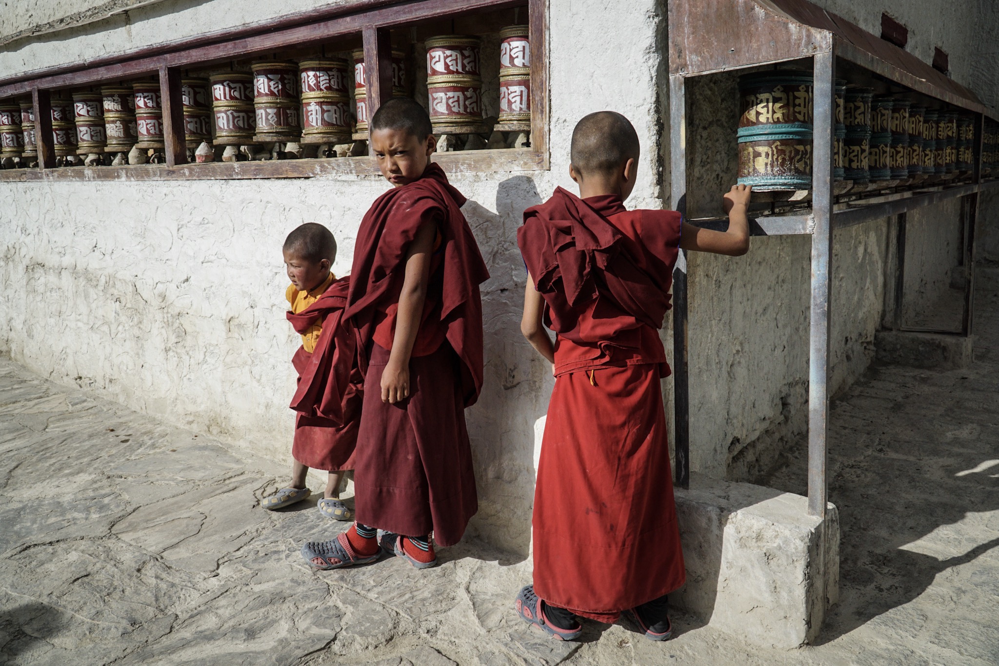 The boys stop at the monastery’s old prayer wheels, the Himalayan sun is strong and sharp.