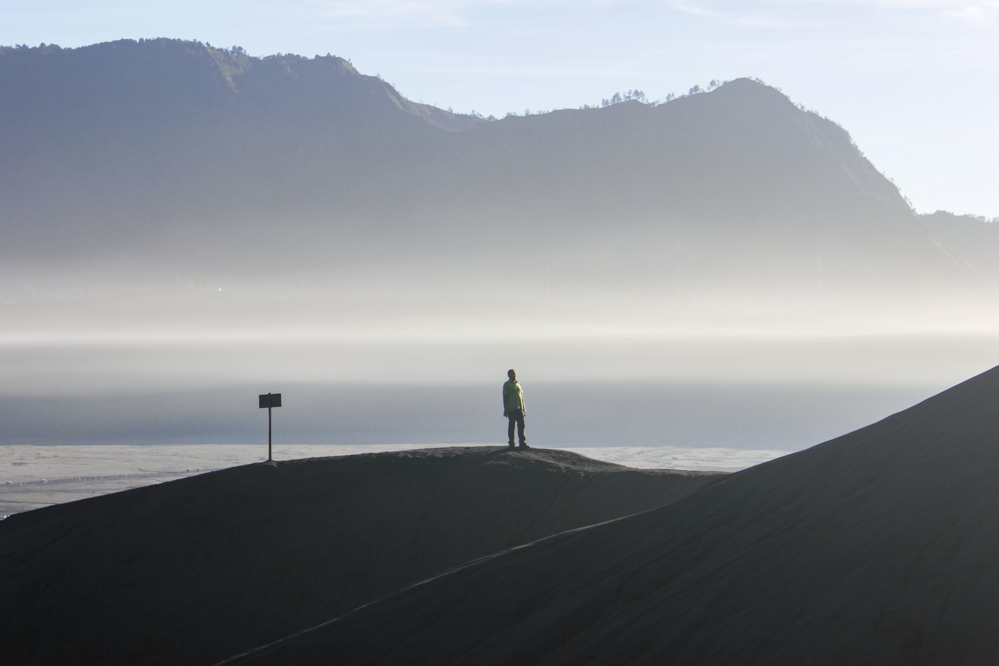 Mount bromo sits inside the massive Tengger caldera (diameter approximately 10 km), surrounded by the Laut Pasir (Sea of Sand) of fine volcanic sand.(in frame: man standing in middle of sea of sand)