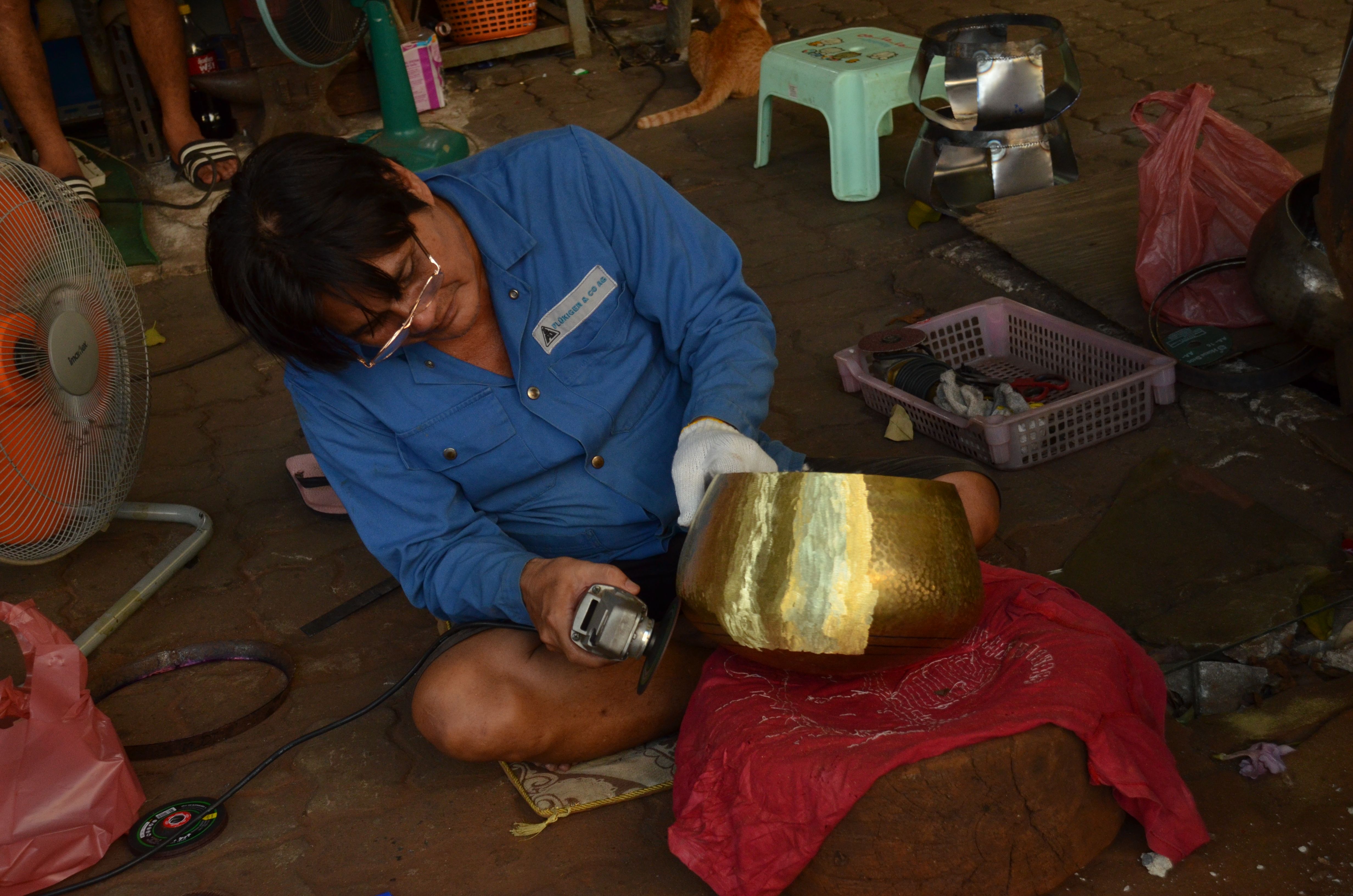 An award-winning craftsman polishes a bowl near Ban Bat. These handmade alms bowls are created by beating strips of copper into shape. 