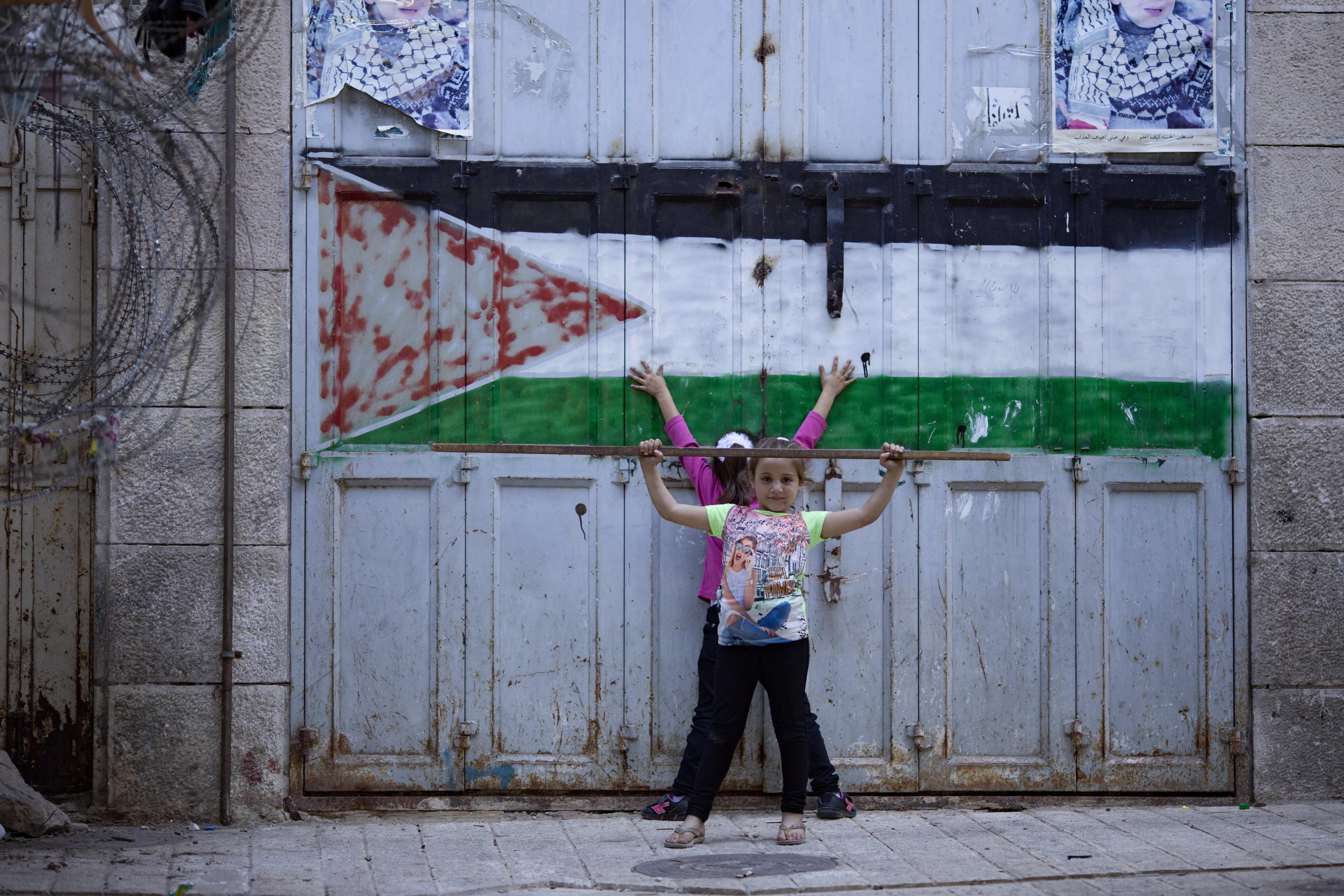 Two Palestinian children pose next to their flag in the closed market area of Hebron. 