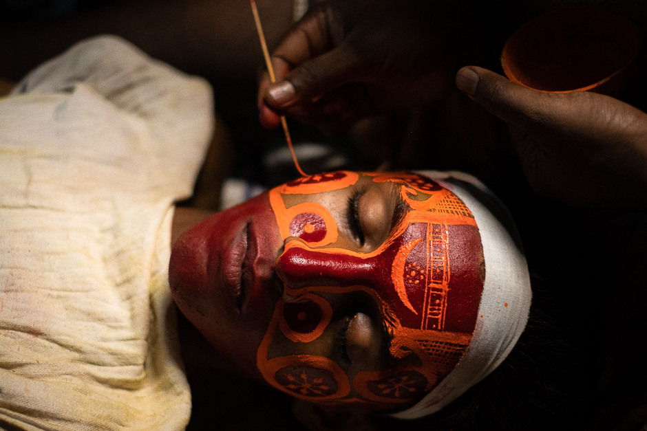 The Painted God.
Theyyam is a centuries-old dance form practiced in the northern districts of Kerala, where the dancer is believed to transform into a deity during the performance. Pictured here is a Theyyam dancer, lying still, as an intricate make up is painstakingly applied on his face.