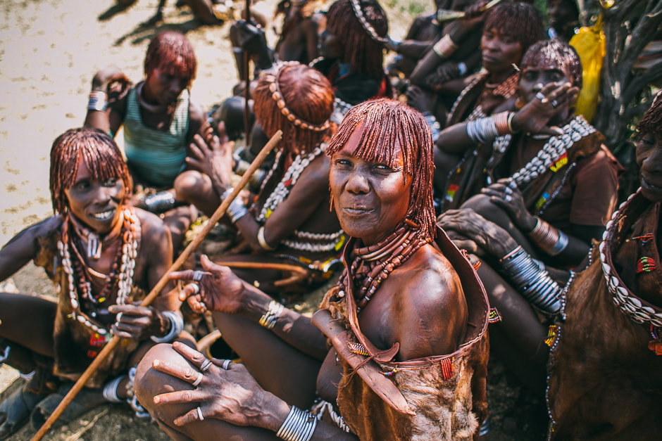 The women relax in the sun with their skin and hair glistening from the mixture of ochre and butter, taking a break from the singing and playing of their horns. 