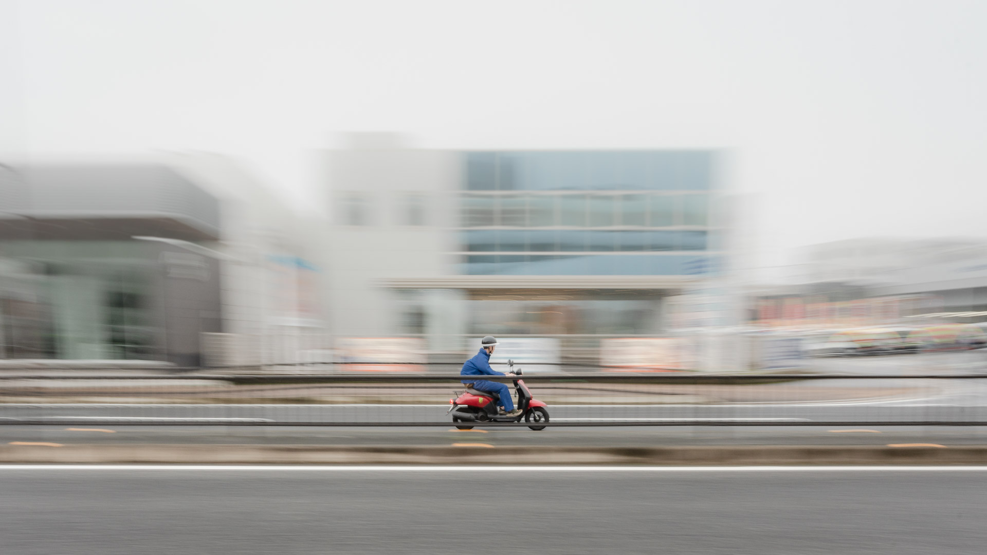 A typical Japanese factory worker seen riding a typical Japanese scooter wearing a typical Japanese  helmet across a typical neighbourhood in Kitakyushu Japan.